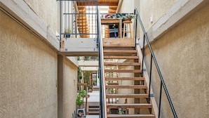 Een smal, meerlaags interieur met een houten trap, een balkon en uitzicht op buiten.