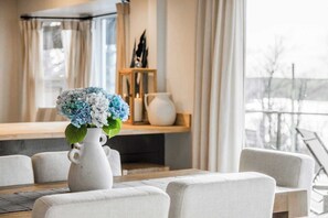 A modern dining area with a white vase of flowers, a wooden sideboard, and a view of the outdoors. - The Golden Hour Overlook at Beaver Lake (Rogers)