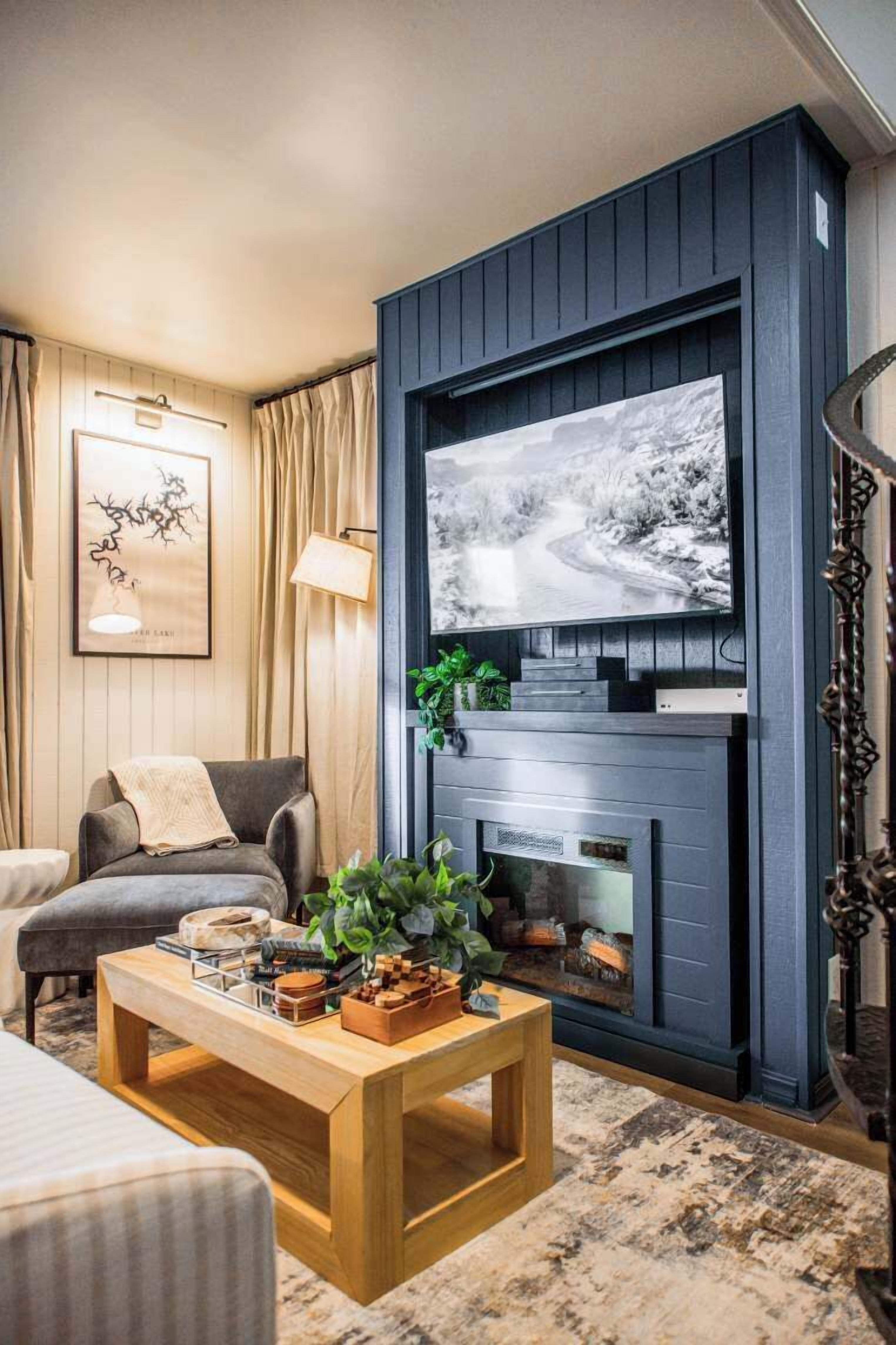 A living room with a fireplace, a television mounted on a dark wall, a sofa, a coffee table, and a framed picture on the wall.