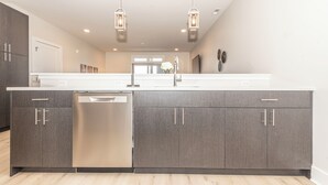 A modern kitchen with a dishwasher, double doors, and pendant lighting. - NEW Upscale Pool View Condo - Walk to Outlets + Near Beaches (Rehoboth Beach)