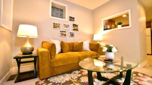 Una sala de estar con un sofá, dos lámparas, una mesa de centro de vidrio y una alfombra estampada.