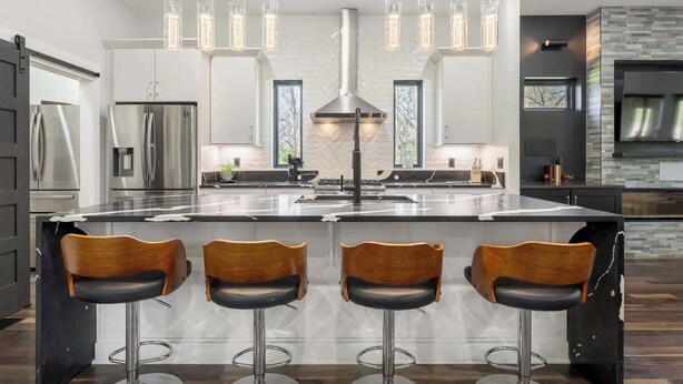 Een moderne keuken met roestvrijstalen apparatuur, een centraal eiland met barstoelen, hanglampen en een achterwand van steen.