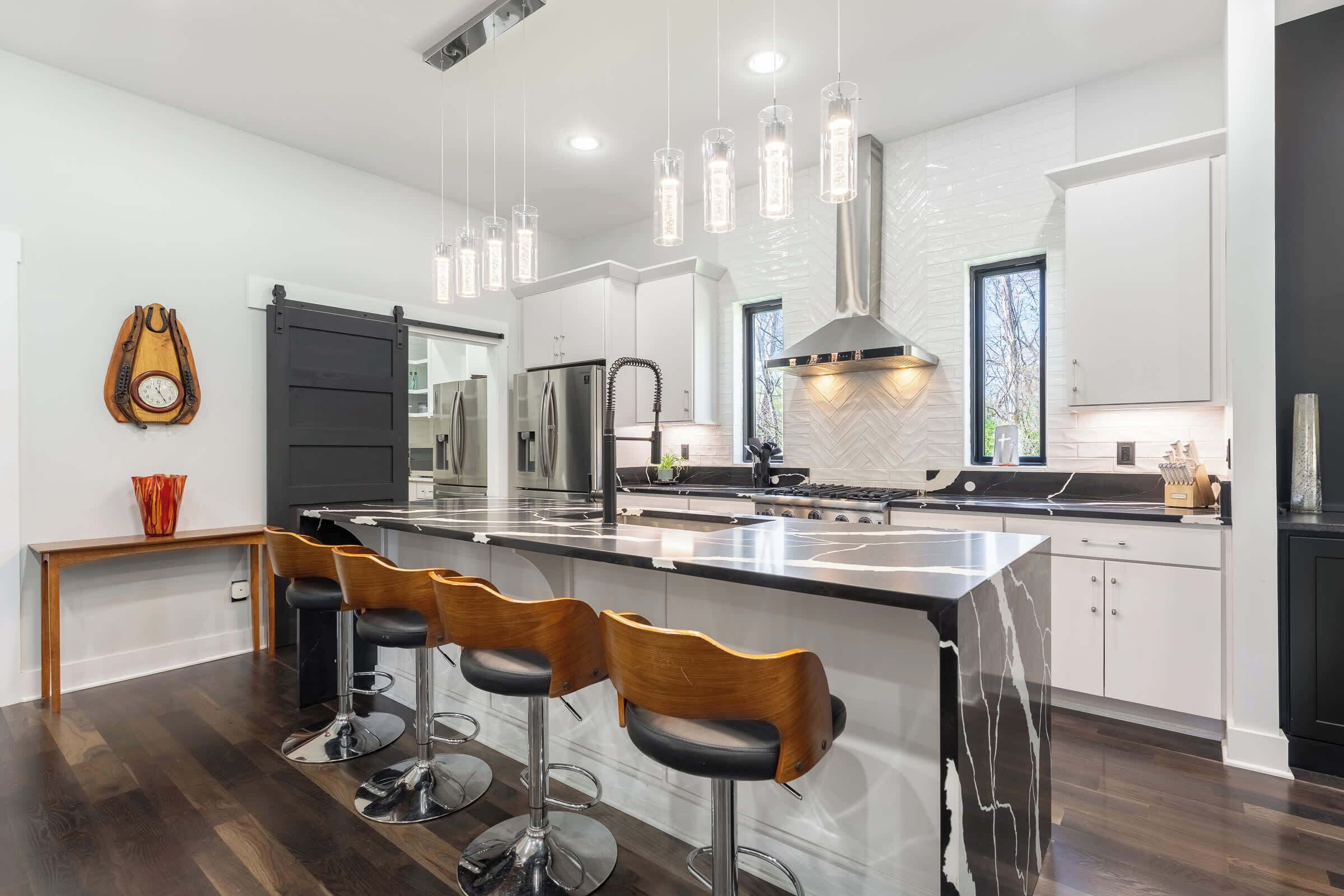 Una cocina moderna con una isla central, taburetes de bar, electrodomésticos de acero inoxidable e iluminación colgante.