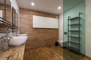 Een badkamer met een witte wastafel, een spiegel, een bakstenen muur en een douchecabine van glas.