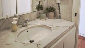 A bathroom with a marble sink, two towels hanging on a towel rack, a mirror, and two potted plants on the counter. - Cozy Suite in Bairro Alto Shared House (Lisboa)