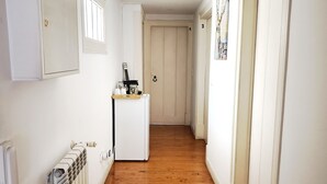 A narrow hallway with wooden flooring, white walls, a radiator, a small refrigerator, and a door marked with the number 2. - Cozy Suite in Bairro Alto Shared House (Lisboa)