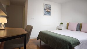 A bedroom with a bed, a desk, a chair, a nightstand, a lamp, and a wall-mounted picture. - Cozy Suite in Bairro Alto Shared House (Lisboa)