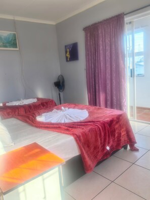 Una habitación de hotel con una cama, un ventilador, una ventana con cortinas y un cuadro en la pared.