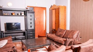 A living room with a sofa, a coffee table, a television, and a wardrobe. - Affordable Guest House in Goodwood (Cape Town)
