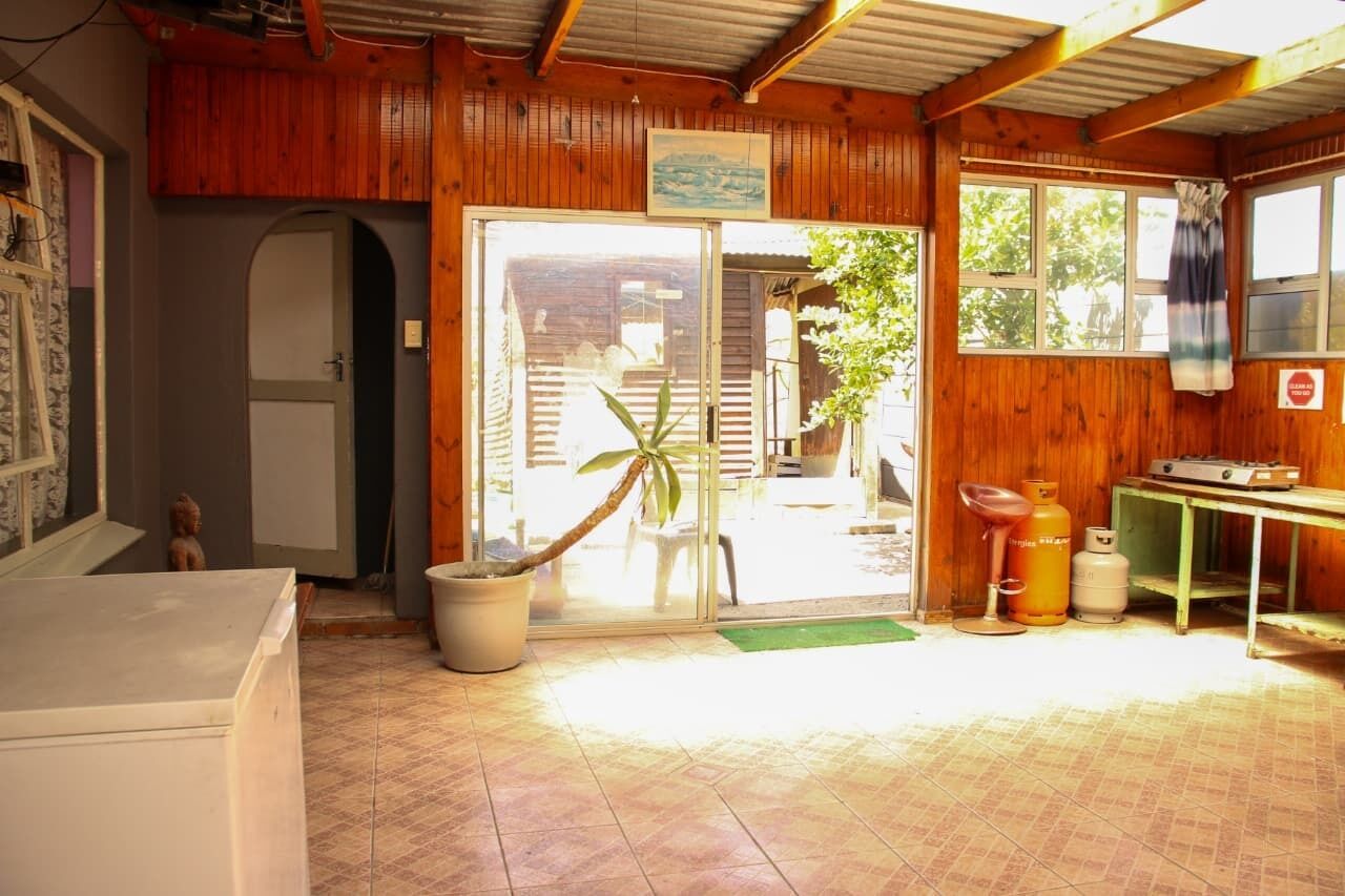Un intérieur en bois avec une porte-fenêtre coulissante donnant sur l’extérieur, une petite table avec des bouteilles de gaz et un tapis vert à l’entrée.