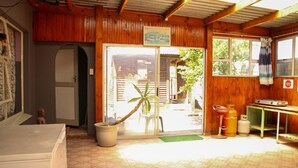 A wooden interior with a sliding glass door leading outside, a small table with gas cylinders, and a green mat at the entrance. - Affordable Guest House in Goodwood (Cape Town)