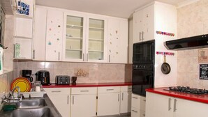 A kitchen with white cabinets, a red countertop, a black oven, and a stainless steel sink. - Affordable Guest House in Goodwood (Cape Town)