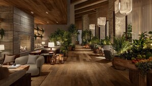 A spacious lobby with wooden flooring, a fireplace, multiple seating areas, and various potted plants.