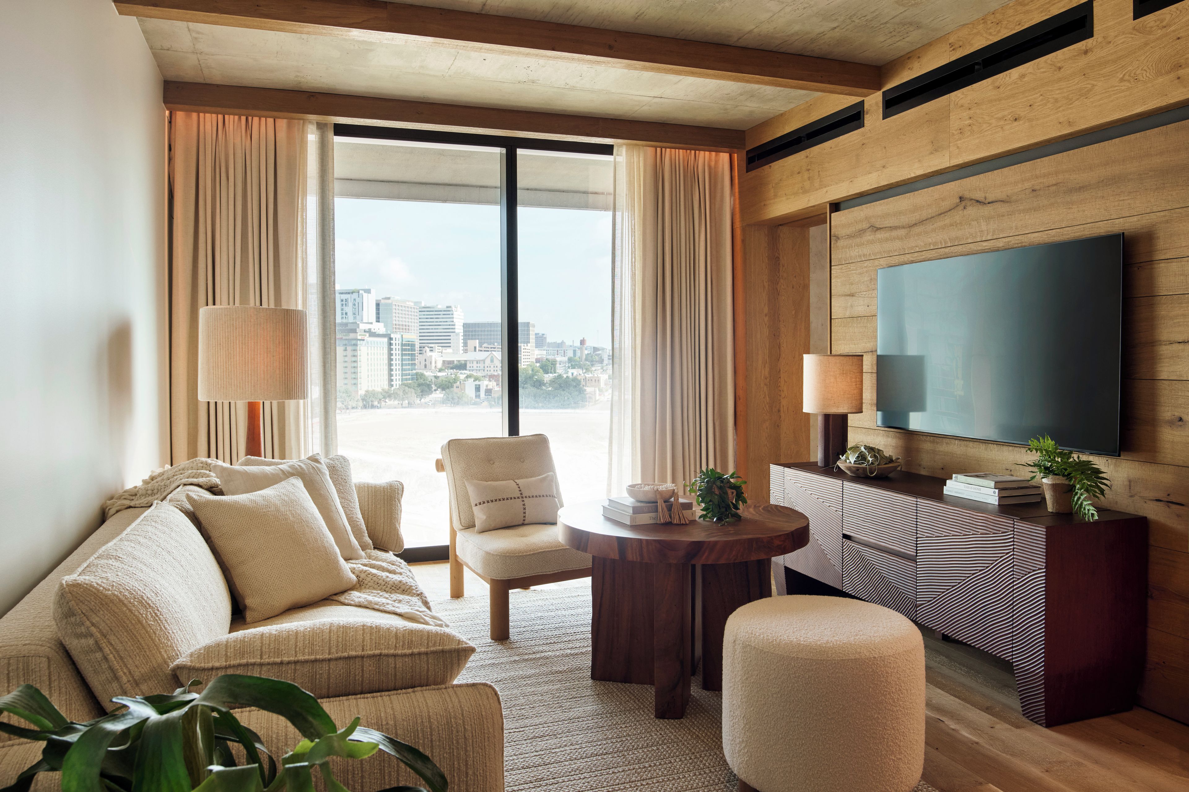 Een moderne hotelkamer met een groot raam, een bank, een stoel, een kleine tafel en een televisie aan de muur.