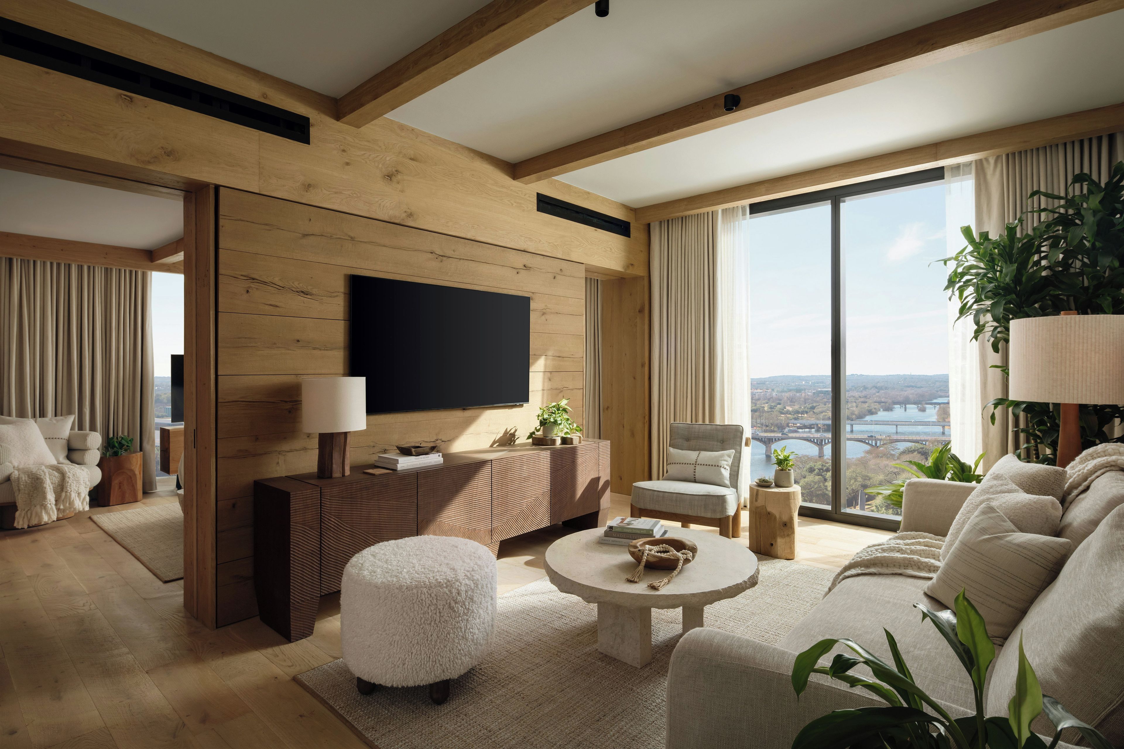 Een moderne woonkamer met een grote televisie, houten balken, een bank, een salontafel en uitzicht op een brug.