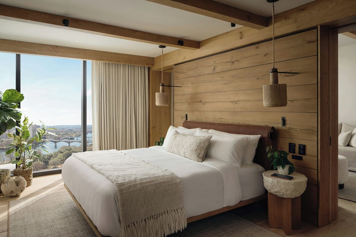 A modern bedroom with a large bed, wooden beams, a view of a bridge, and a potted plant.