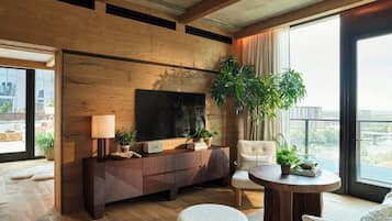 A modern living room with a large TV, wooden panel walls, a sofa, a round coffee table, and a view of the city.