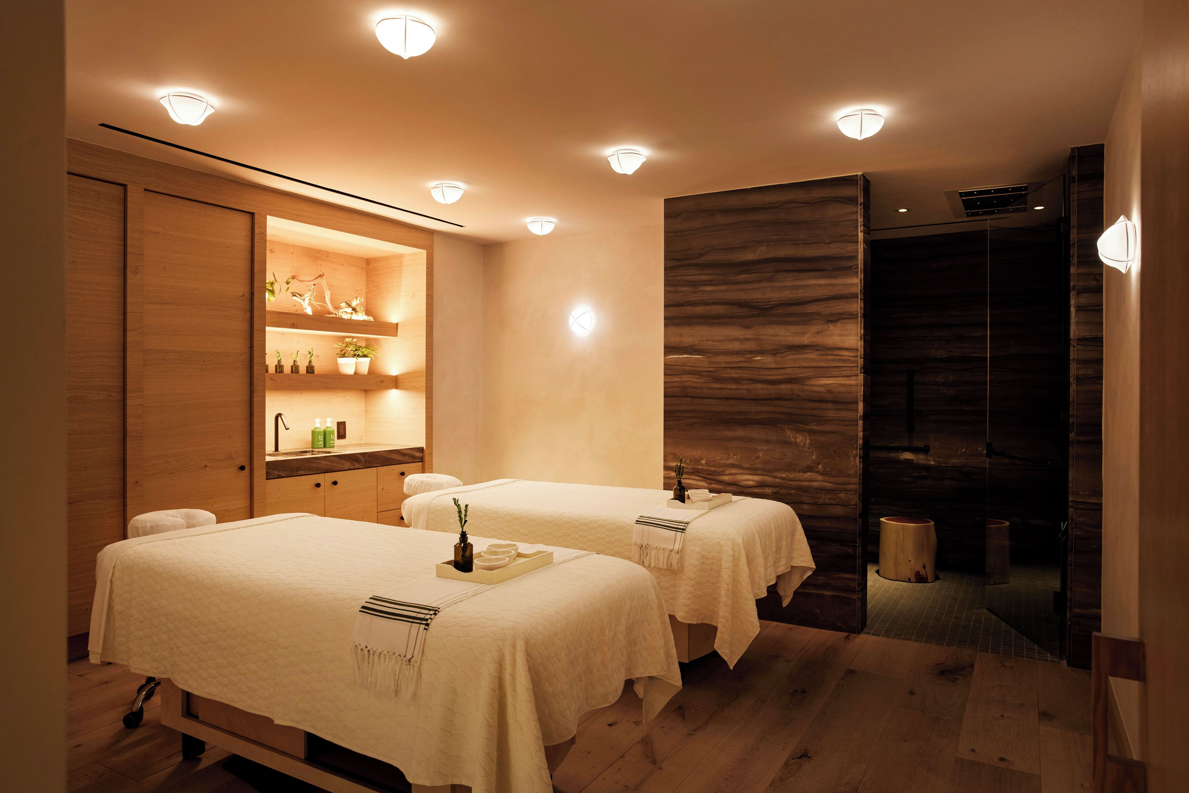 A spa room with two treatment beds, wooden cabinets, and a mirror.