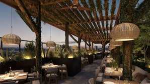 An outdoor dining area with tables and chairs, overhead lighting, and greenery.