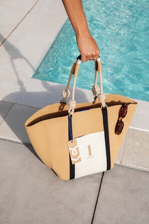 Een hand houdt een geweven strandtas met een label waarop 'Rothys Hotels' staat.