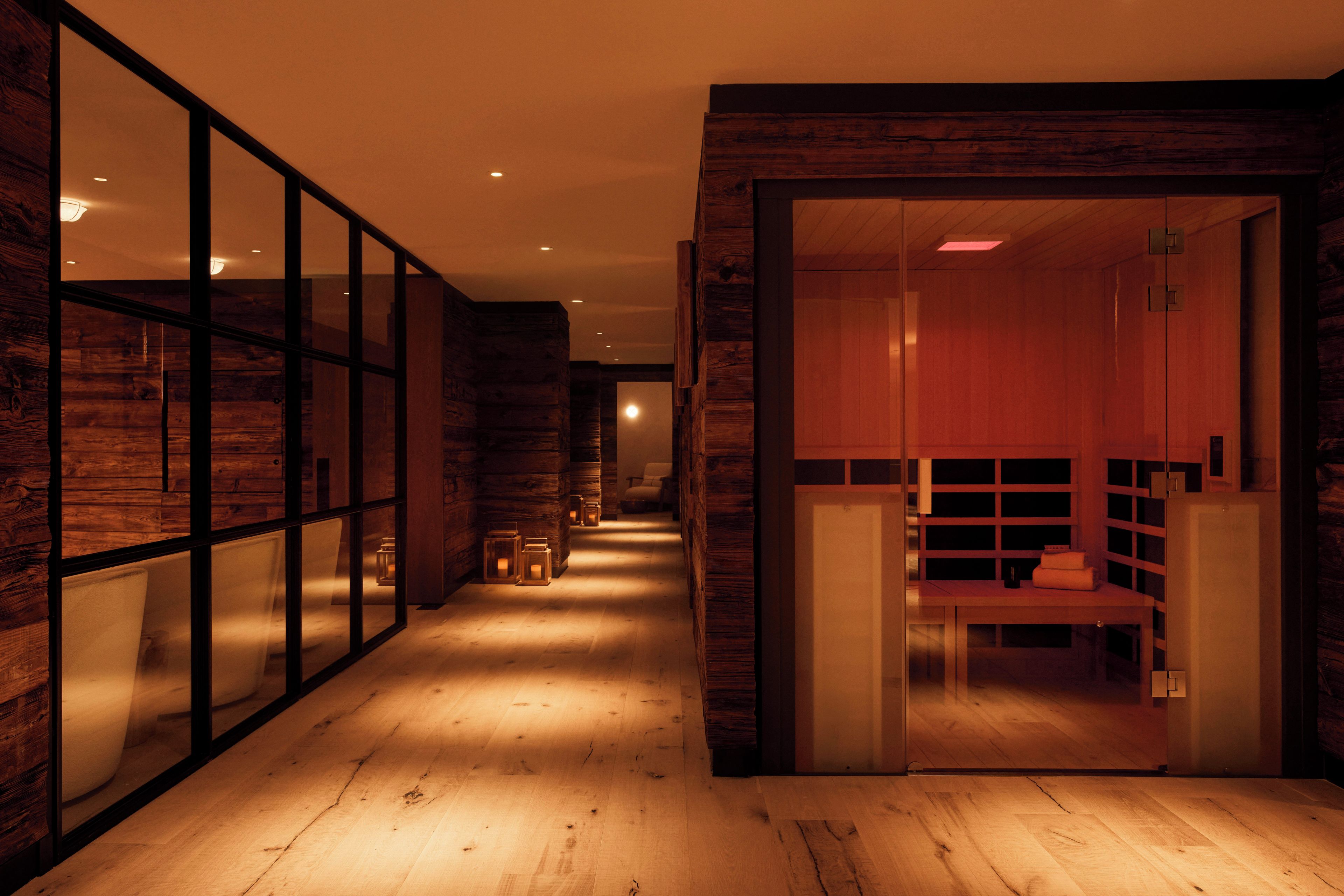 A hallway with wooden walls and a glass partition, leading to a room with a wooden bench and a small table.