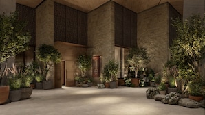 A hotel lobby with a modern design, featuring a large wooden ceiling, stone walls, and numerous potted plants.