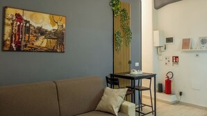 Ein Wohnzimmer mit einer Couch, einem Tisch mit Stuhl, einer Wandpflanze und einem Gemälde.