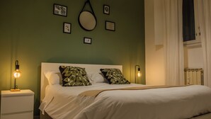 Ein ordentlich bezogenes Bett mit weißer Bettwäsche, zwei Nachttische mit Lampen und eine Wand mit gerahmten Bildern.