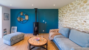 Ein Wohnzimmer mit einer Couch, einem runden Holztisch, einer blauen Wand, einer Steinwand und einem schwarzen Heizkörper.