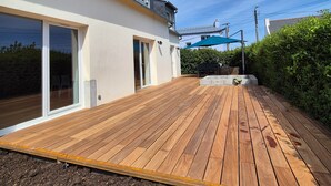 Eine Holzterrasse mit einer Schiebeglastür, einem blauen Sonnenschirm und einem Steingartenbehälter.