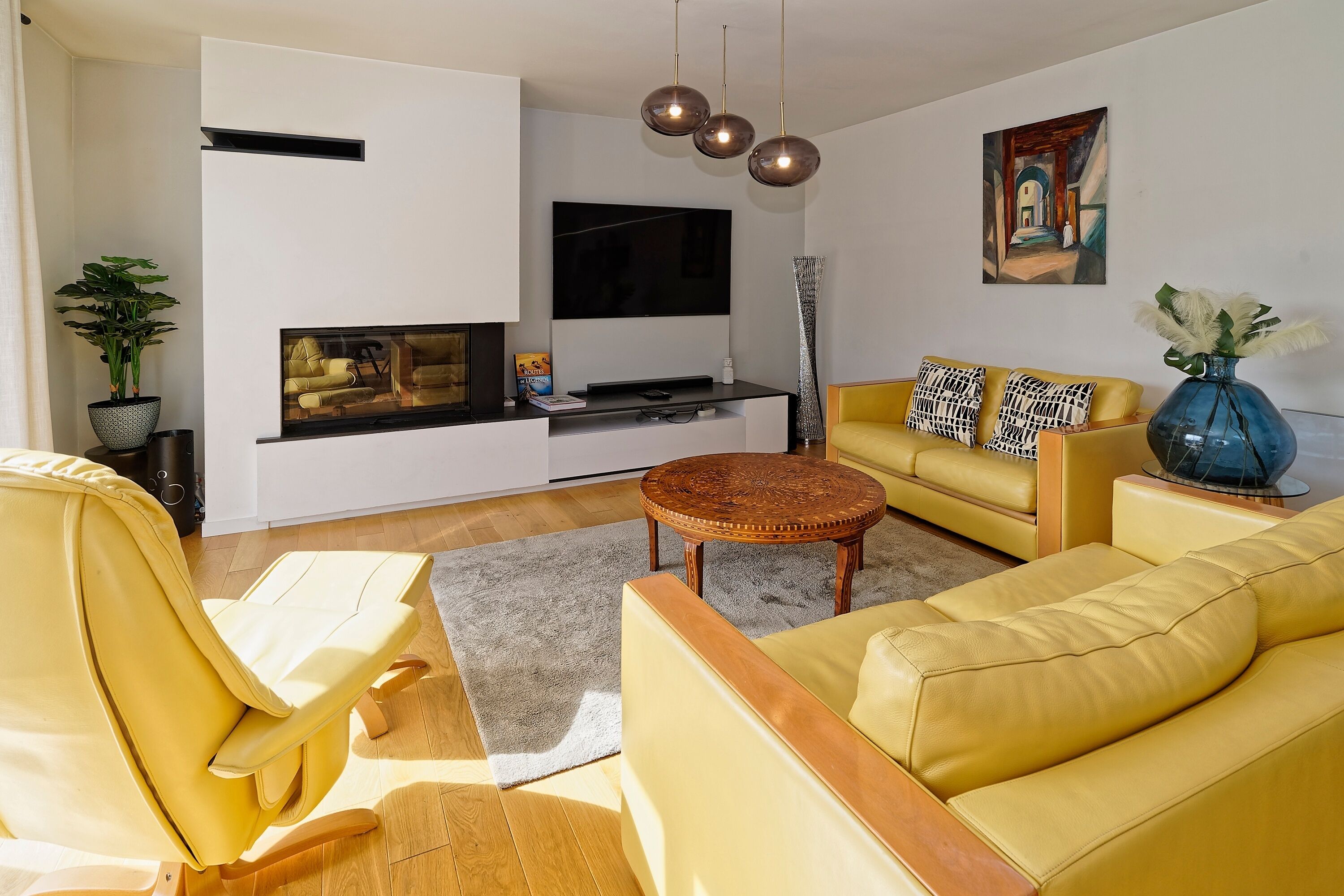 A modern living room with a yellow sofa, a coffee table, and a flat-screen TV mounted on the wall.