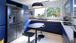 Una cocina moderna con refrigerador empotrado, una mesa de comedor redonda y un ventanal con vistas a palmeras.