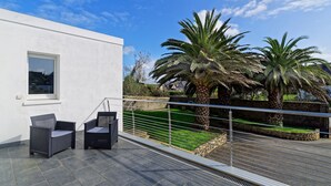 Un patio moderno con dos sillas de mimbre, una pared blanca y vistas a un jardín con palmeras.