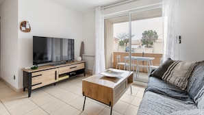A modern living room with a flat-screen TV, wooden furniture, a glass coffee table, and a balcony with a view. - La Brise d'Agde - 3km de la Plage (Agde)