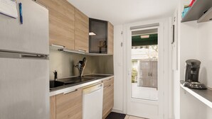 A compact kitchen with a dishwasher, a coffee machine, and a door leading to an outdoor area. - La Pause Valrassienne - 1km de la Plage (Valras-Plage)