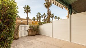 A paved patio area with a white gate, a white fence, and palm trees in the background. - La Pause Valrassienne - 1km de la Plage (Valras-Plage)