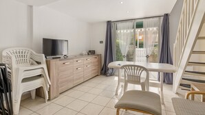 A modern kitchen with a TV, wooden cabinets, and a dining area with chairs. - La Pause Valrassienne - 1km de la Plage (Valras-Plage)