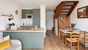 Cozinha moderna com ilha central, área de jantar com cadeiras de madeira e escada para um andar superior.
