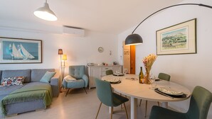 Ett modernt vardagsrum med en soffa, ett matbord med stolar, en lampa och en inramad tavla på väggen.