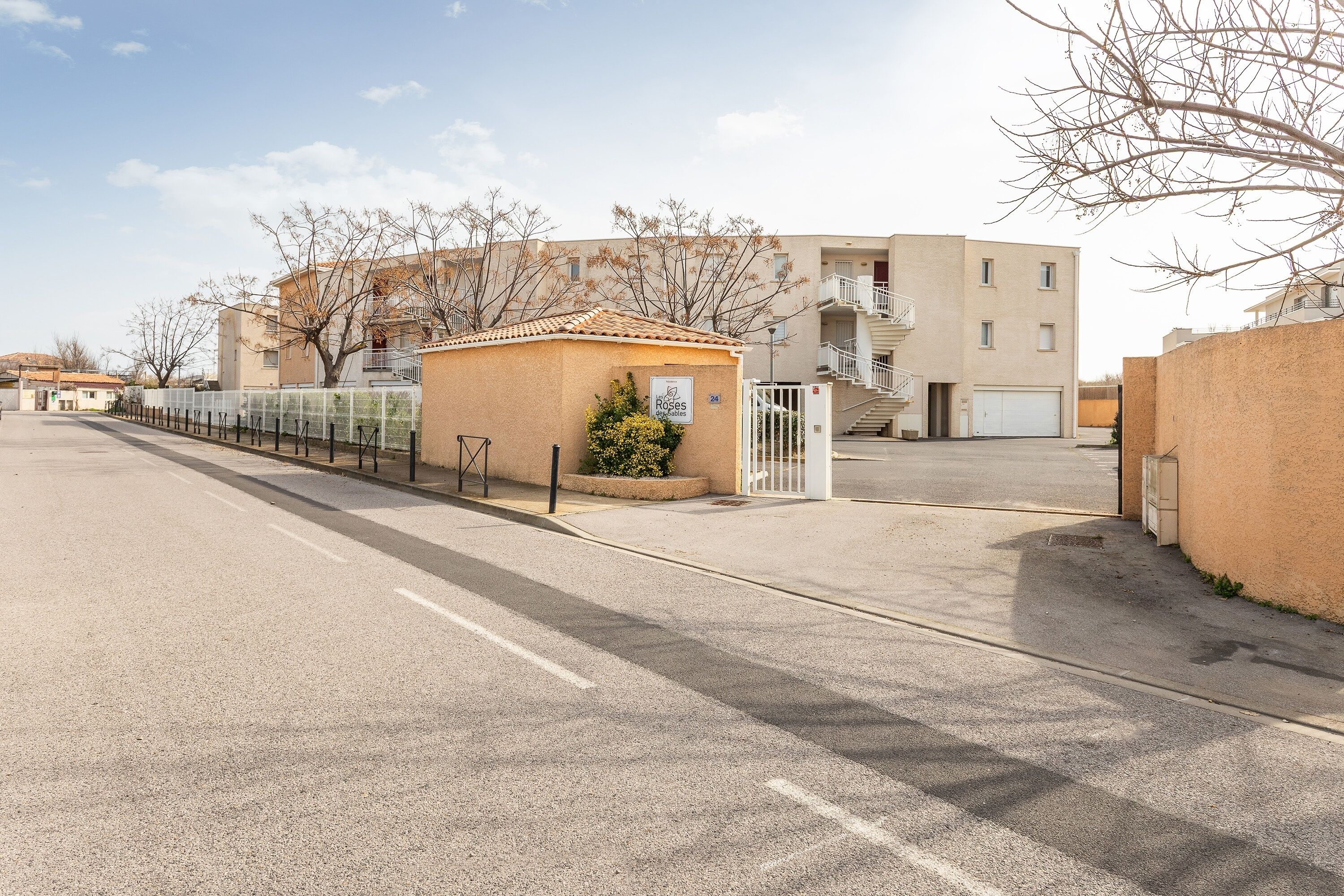 A parking lot with a gated entrance, a small building with a sign, and a multi-story residential building in the background.