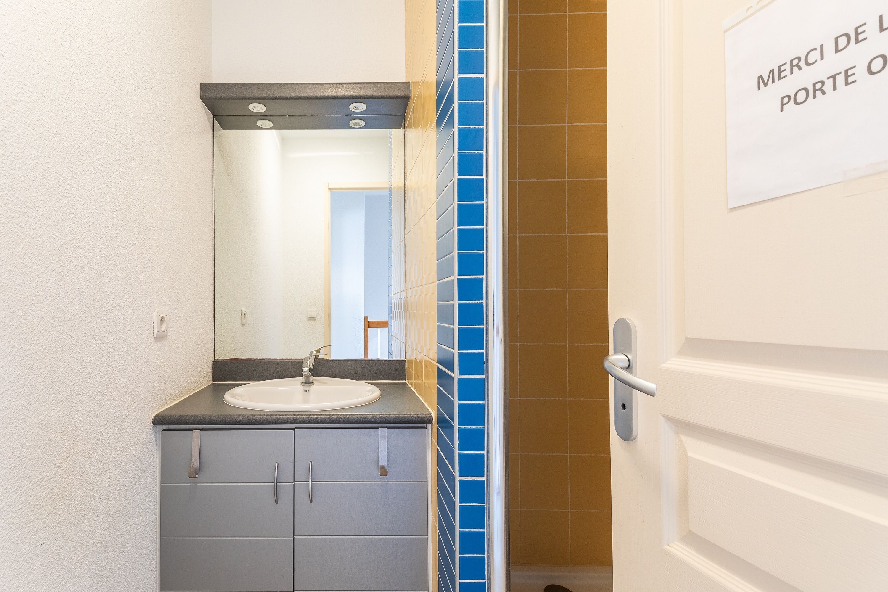 A bathroom with a sink, mirror, and a door with a sign.