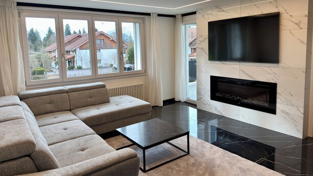 Ein modernes Wohnzimmer mit einer Eckcouch, einem Flachbildfernseher, einem Kamin und großen Fenstern.