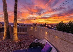 Ein Sonnenuntergangsblick von einem Balkon mit Palmen, einem Korbstuhl und einer Steinmauer.