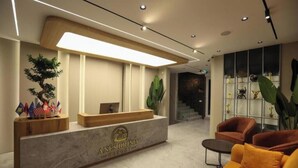 A reception desk with a logo, a wooden counter, a plant, and a seating area with chairs. - Resort Anës Drinit  (Radac)