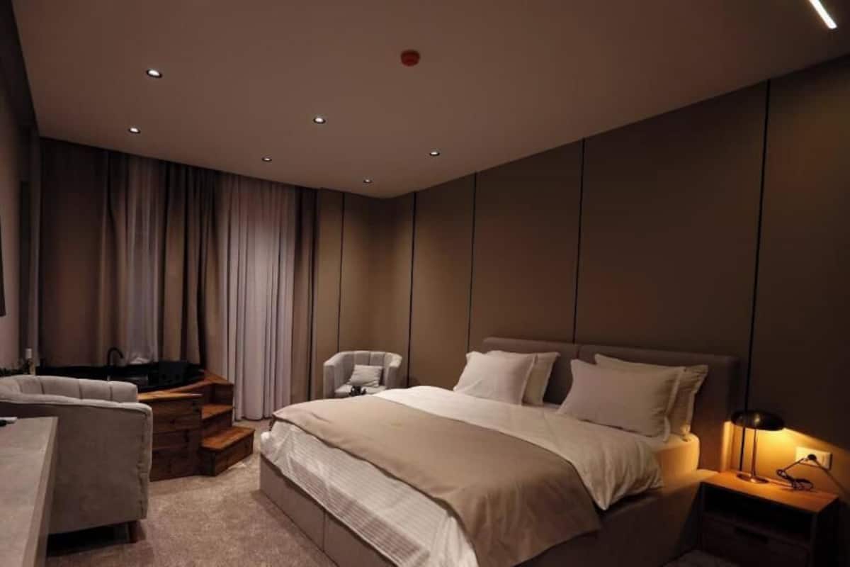 A modern bedroom with a large bed, bedside tables, a desk, and a chair.