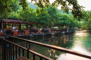 Restaurante à beira do rio com mesas ao ar livre, um deck de madeira e vista para a água.