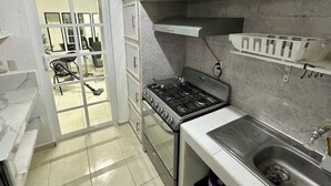Une cuisine compacte avec des meubles blancs, une cuisinière à gaz, un évier et un petit plan de travail.