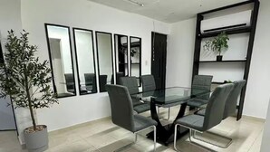 Une salle de conférence avec une table en verre, quatre chaises, une plante en pot et une étagère sur laquelle est posée une autre plante.