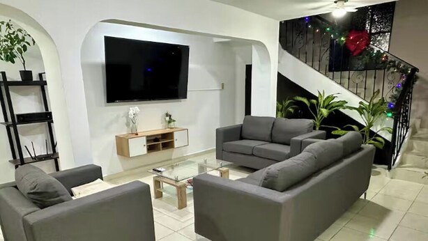 Un salon moderne avec un canapé gris, un téléviseur à écran plat, un meuble en bois et un escalier décoré pour les fêtes.
