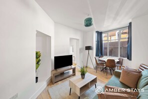 A modern living room with a flat-screen TV, a sofa, a coffee table, and a dining area with chairs and a table. - 234 Birstol Rd Apt, Gloucester (Gloucestershire)